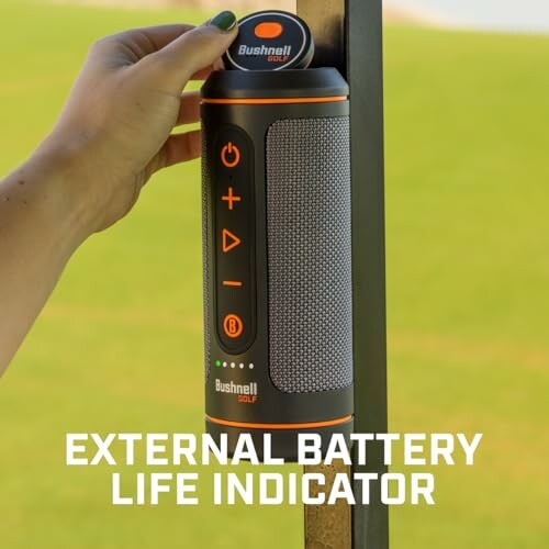 Person holding Bushnell golf speaker with external battery life indicator.