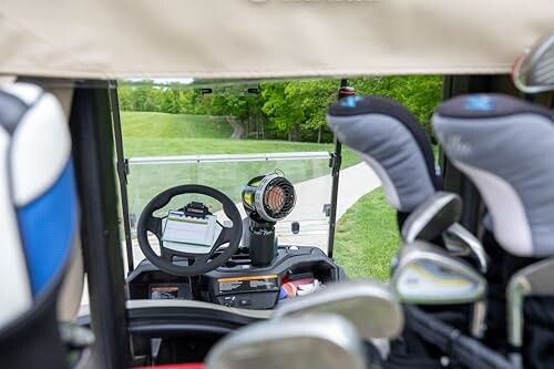 View from inside a golf cart with golf clubs and a course path ahead.