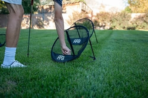 Person setting up a golf net on a lawn.